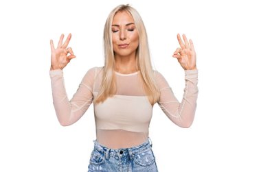 Gündelik kıyafetler giyen genç sarışın kadın rahatla ve gözleri kapalı gülümse parmaklarıyla meditasyon hareketi yapıyor. yoga konsepti. 