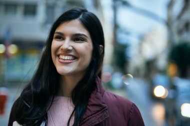 Genç İspanyol kız gülümseyerek şehirde mutlu mesut dikiliyor..