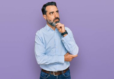 Orta yaşlı, sakallı, iş gömleği giyen, çenesi üzerinde soru soran, düşünceli bir adam. Düşünceli bir yüzle gülümsüyor. şüphe kavramı. 