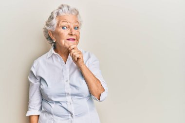 Üstün gri saçlı, günlük kıyafetler giyen, kameraya gülümseyen, kollarını çapraz yapıp çenesine dokunan bir kadın. Olumlu düşünmek. 