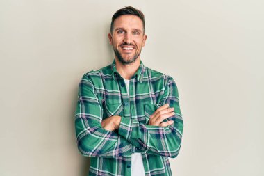 Sakallı, sıradan giyinen, mutlu yüzlü, kollarını kavuşturup kameraya bakan yakışıklı bir adam. pozitif kişi. 