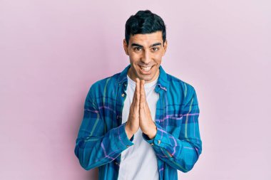 Yakışıklı İspanyol adam gündelik giysiler içinde elele dua ederek af diliyor kendinden emin gülümsüyor.. 