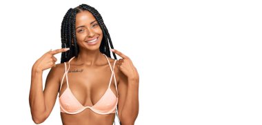 Güzel İspanyol kadın bikini giyip neşeli bir şekilde gülümsüyor ve parmaklarıyla ve ağzıyla işaret ediyor. diş sağlığı kavramı. 