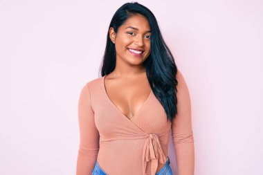 Güzel, uzun saçlı, günlük kıyafetler giyen, pozitif ve mutlu görünen, kendine güvenen, gülümseyen, dişlerini gösteren güzel bir Latin kadın. 