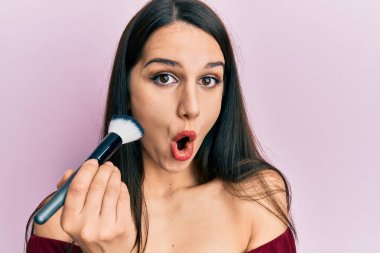 Makyaj fırçası tutan, yüzü kızaran, ağzı açık, korkmuş, şaşkın, ağzı açık genç bir kadın. 