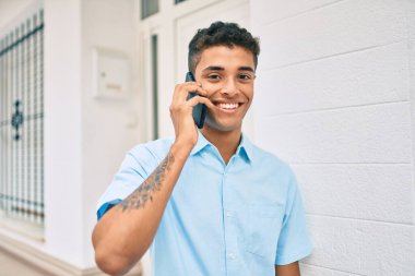 Genç Latin adam gülümsüyor ve şehirde akıllı telefondan konuşuyor..