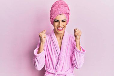 Başında duş havlusu ve bornoz olan genç adam zafer kutlamaları için kollarını kaldırmış ve gözlerini kapatmış gülümsüyor. Kazanan konsept. 