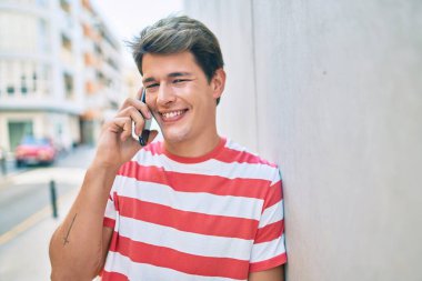 Genç beyaz adam gülümsüyor. Şehirdeki akıllı telefondan konuşuyor..