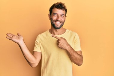 Sarı arka planda sıradan sarı tişörtler giyen sakallı yakışıklı adam kameraya hayret ediyor ve gülümsüyordu.. 