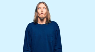 Handsome caucasian man with long hair wearing casual winter sweater making fish face with lips, crazy and comical gesture. funny expression. 
