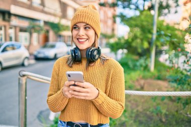 Şehirde akıllı telefon ve kulaklık kullanan genç sarışın kadın..