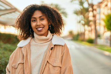 Genç Afrikalı Amerikalı kadın gülümseyerek şehirde mutlu mesut duruyor..