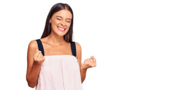 Gündelik kıyafetler giyen genç İspanyol kadın başarı için heyecanlı kolları havada ve gözleri kapalı zaferi kutlarken gülümsüyor. Kazanan konsept. 