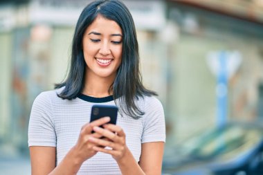 Genç İspanyol kadın şehirde akıllı telefon kullanarak mutlu bir şekilde gülümsüyor..