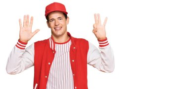 Beyzbol üniforması giyen yakışıklı beyaz adam 8 numarayı gösterip işaret ederken kendinden emin ve mutlu bir şekilde gülümsüyor.. 
