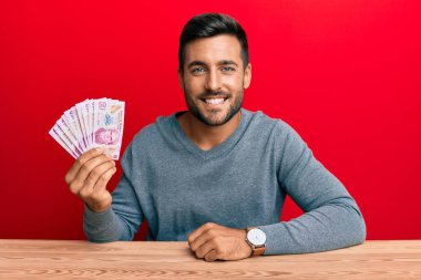 Yakışıklı İspanyol adam Meksika pesolarını tutuyor. Olumlu ve mutlu görünüyor. Kendine güvenen bir gülümsemeyle dişlerini gösteriyor. 