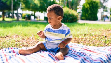Sevimli Afro-Amerikan çocuk parkta çimlerin üzerinde oturuyor..