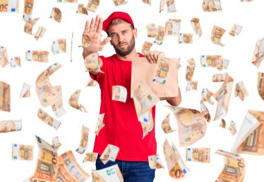 Sarışın, yakışıklı bir adam, elinde bir kese kağıdıyla elinde teslimat çantası, dur işareti yapıyor, ciddi ve kendinden emin bir ifadeyle, savunma hareketi yapıyor.