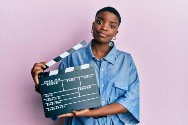 Young african american woman holding video film clapboard relaxed with serious expression on face. simple and natural looking at the camera. 
