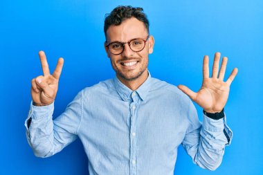 Gündelik kıyafetler giyen ve gözlük takan genç İspanyol adam yedi numaralı parmaklarını gösterip işaret ederken kendine güvenen ve mutlu bir şekilde gülümsüyor.. 