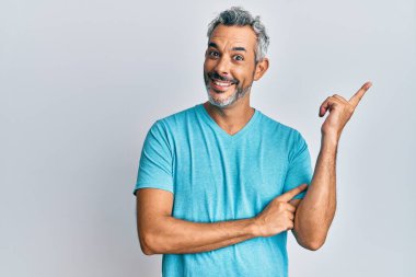 Orta yaşlı, gri saçlı, günlük kıyafetler giyen, yüzünde kocaman bir gülümseme olan, eli ve parmağı kameraya bakan bir adam.. 