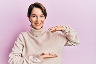 Kısa saçlı genç esmer kadın, sıradan bir kazak giyiyor. Elleri büyük ve büyük beden işareti, ölçü sembolü gösteriyor. Kameraya bakıp gülümsüyor. ölçüm kavramı. 