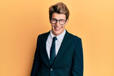 Yakışıklı, beyaz takım elbiseli ve kravatlı bir adam kameraya seksi bir ifadeyle bakıyor, neşeli ve mutlu bir yüzü var.. 