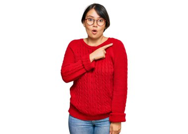 Kısa saçlı, sıradan süveter giyen ve gözlüklü genç, güzel İspanyol bir kadın parmaklarını yana doğru göstererek şaşırmış, ağzı açık, şaşkın bir ifade sergiliyor.. 