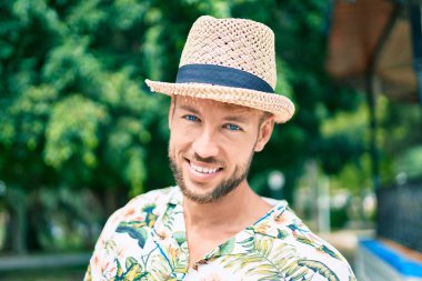 Yazlık şapkalı ve çiçekli tişörtlü yakışıklı beyaz adam dışarıda mutlu gülümsüyor.