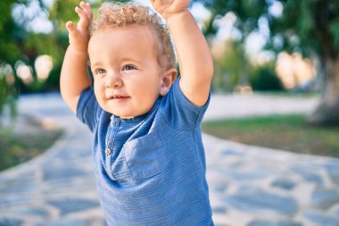 Sevimli ve mutlu küçük çocuk güneşli bir günde parkta eğleniyor. Güzel sarı saçlı erkek çocuk dışarıda oynuyor.