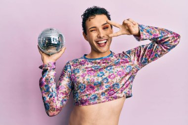 Handsome man wearing make up holding shiny disco ball winking looking at the camera with sexy expression, cheerful and happy face. 