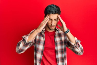 Elleri başının üstünde, günlük kıyafetler giyen genç yakışıklı bir adam. Stres yüzünden başı ağrıyor. migren ağrısı. 