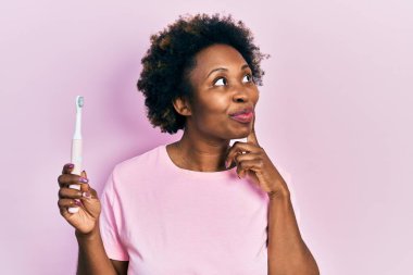 Elektrikli diş fırçası tutan Afrikalı Amerikalı genç bir kadın ciddi bir yüz ifadesiyle eli çenesinde soru sormayı düşünüyor, kafa karıştırıcı bir fikir. 