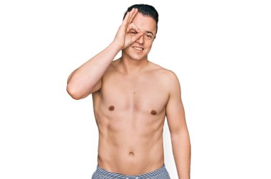 Mayo giyen yakışıklı genç adam el hareketleriyle gülümsüyor ve mutlu yüzüyle parmaklarının arasından bakıyor.. 