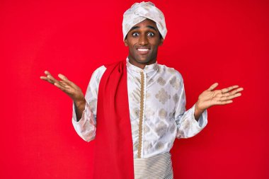 Sherwani sari giysisi giyen yakışıklı Hintli adam. Hiçbir şeyden haberi olmayan, elleri ve kolları havada, kafası karışık bir ifade. şüphe kavramı. 