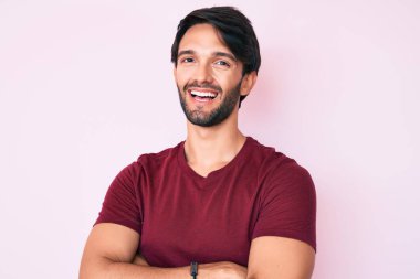 Yakışıklı, sıradan kıyafetler giyen mutlu yüzlü, kollarını kavuşturup kameraya bakan bir İspanyol. pozitif kişi. 