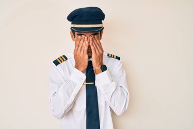 Young hispanic man wearing airplane pilot uniform rubbing eyes for fatigue and headache, sleepy and tired expression. vision problem 