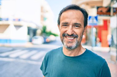 Orta yaşlı, sakallı, açık havada mutlu gülümseyen bir adam.