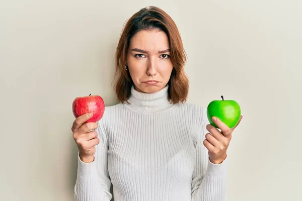 年轻的高加索女人拿着红绿相间的苹果 忧心忡忡 怒气冲冲地哭泣着 悲伤的表情 — 图库照片