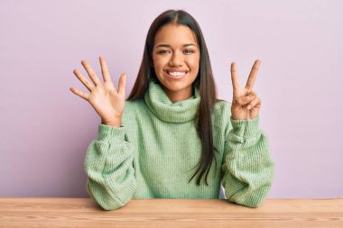 Güzel İspanyol kadın gündelik giysiler içinde masada oturuyor ve yedinci parmaklarını göstererek gülümsüyor ve mutlu.. 
