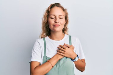 Güzel, beyaz bir kadın, günlük kıyafetler giyiyor, elleri göğsünde, gözleri kapalı gülümsüyor ve yüzünde minnet ifadesi var. sağlık kavramı. 