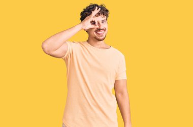 Kıvırcık saçlı, sıradan giyinen, mutlu gülümseyen, el pençe divan duran yakışıklı bir adam. 