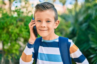 Sevimli beyaz çocuk gülümsüyor. Parktaki akıllı telefondan konuşuyor..