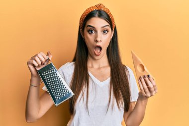 Güzel esmer, elinde rende ve peynir tutan genç bir kadın şaşkınlık ve şaşkınlık dolu bir ifade, korku ve heyecan dolu bir yüz.. 