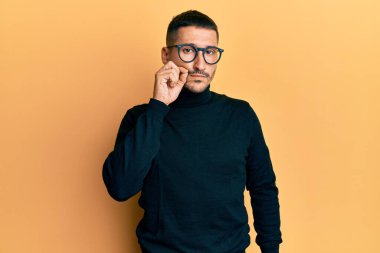 Balıkçı yaka kazak, gözlük takan ağzı ve dudakları parmakları fermuarlı yakışıklı bir adam. gizli ve sessiz, tabu konuşması 