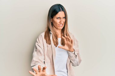 Esmer, sıradan kıyafetler giyen, tiksindirici ifadeler takınan, tiksindirici, tiksindirici yüz ifadeleri olan genç bir kadın. Eller havada. 