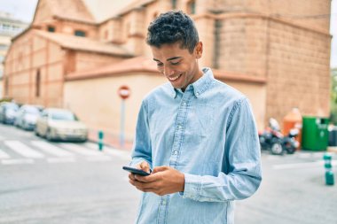 Genç Latin adam mutlu bir şekilde gülümsüyor ve şehirde akıllı telefon kullanıyor..