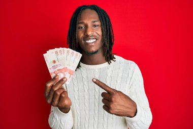 Saçları örgülü, elinde 10 Kolombiya pezosu olan, mutlu bir gülümsemeyle elini ve parmağını gösteren Afro-Amerikan bir adam. 