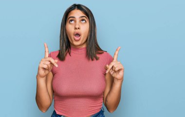 Gündelik tişört giyen genç İspanyol kız şaşırmış ve şaşırmış bir şekilde yukarı baktı ve parmaklarıyla işaret etti ve kollarını kaldırdı.. 