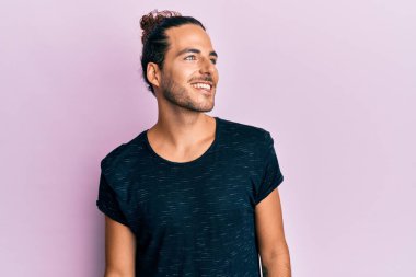 Uzun saçlı, sıradan kıyafetler giyen, yüzünde gülümseme ve doğal ifadeyle yan yana bakan yakışıklı bir genç. Kendinden emin gülen. 